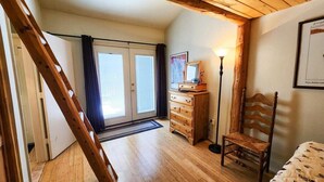 Een kamer met een houten vloer, een houten stoel, een dressoir, een lamp en een lijst met een afbeelding aan de muur.