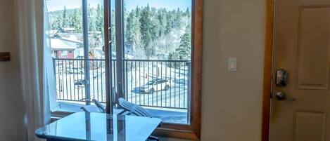 A room with a large window overlooking a balcony with a view of trees and a parking area.