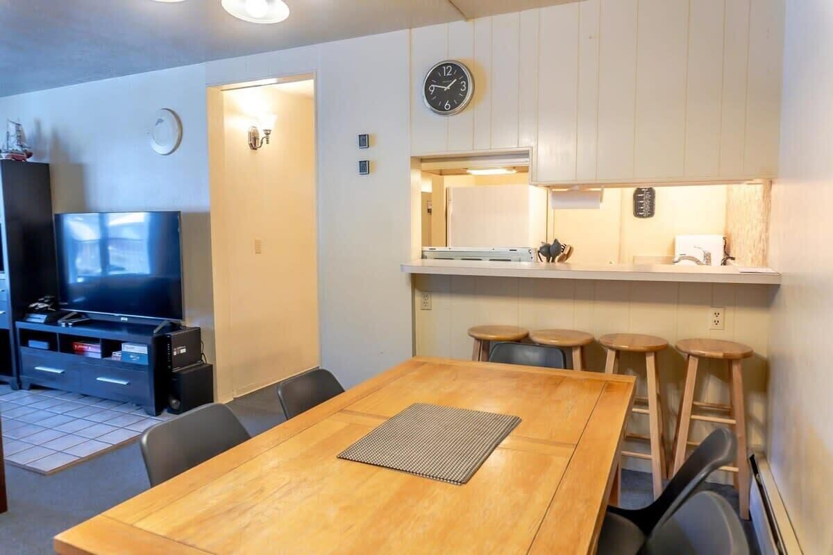 Un espacio habitable compacto con una mesa de comedor de madera, un televisor y una kitchenette.