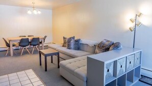 Ein modernes Wohnzimmer mit einer Couch, einem Esstisch mit Stühlen, einem Couchtisch, einer Stehlampe und einem Stauraum.