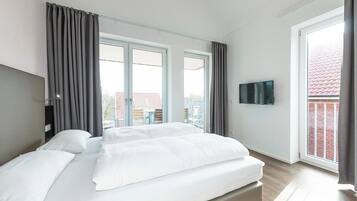 Ein modernes Hotelzimmer mit einem großen Bett, zwei Fenstern, einem Flachbildfernseher und einem Balkon mit Blick auf Gebäude.