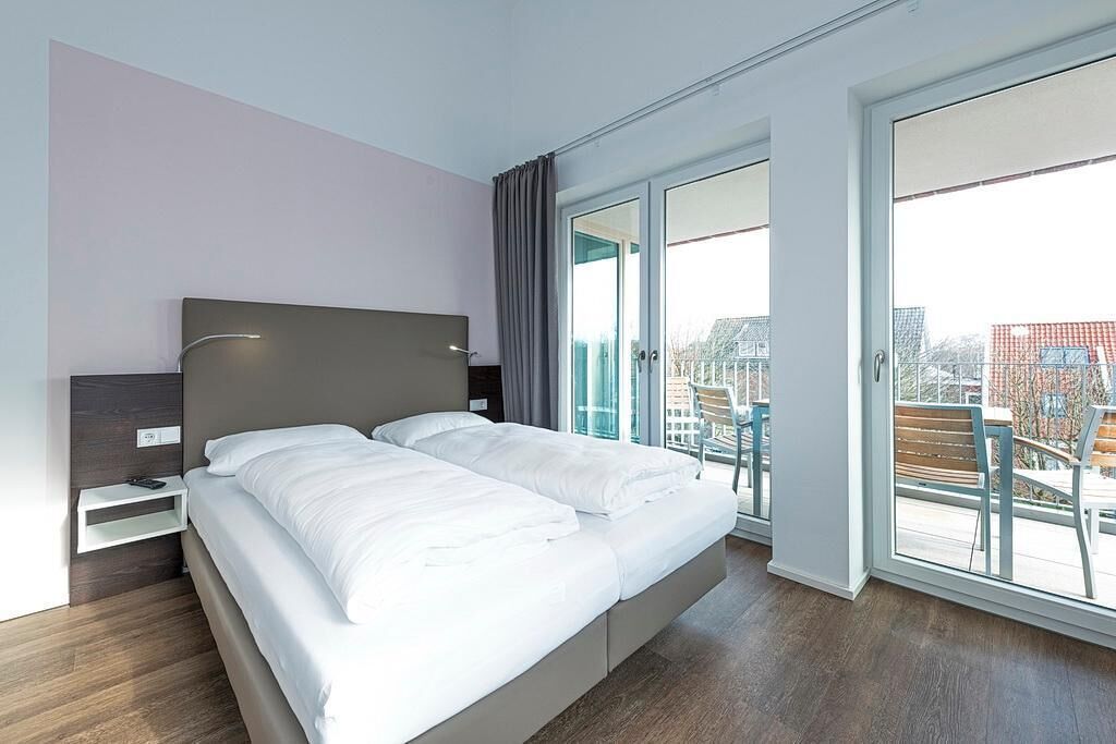 Ein modernes Hotelzimmer mit einem großen Bett, einem Nachttisch und Blick auf die Stadt durch große Fenster.