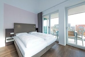 Une chambre d’hôtel moderne avec un grand lit, une table de chevet et une vue sur la ville grâce à de grandes fenêtres.