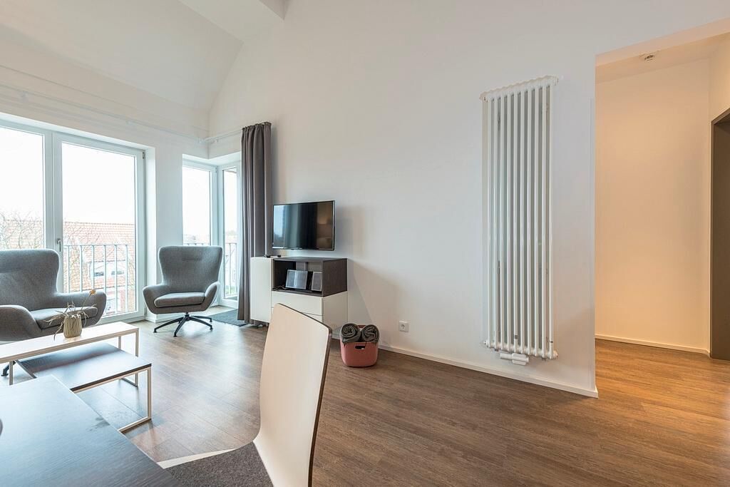 Ein modernes Wohnzimmer mit einem Flachbildfernseher, zwei grauen Sesseln, einem weißen Sofa und Holzboden.