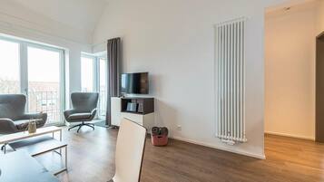 Ein modernes Wohnzimmer mit einem Flachbildfernseher, zwei grauen Sesseln, einem weißen Sofa und Holzboden.