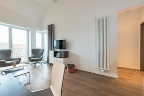 Una sala de estar moderna con un televisor de pantalla plana, dos sillones grises, un sofá blanco y piso de madera.