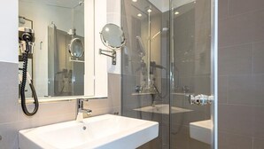 A modern bathroom with a glass-enclosed shower, a white sink, and a handheld mirror.