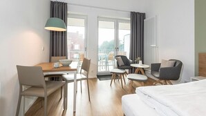 A modern hotel room with a wooden dining table, two chairs, a sofa, a small round table, and a bed.