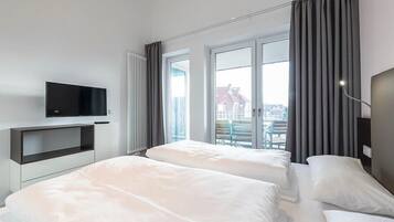 Ein modernes Hotelzimmer mit zwei Betten, einem Flachbildfernseher und großen Fenstern mit Vorhängen.