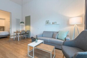 Un salon moderne avec un canapé gris, une table basse blanche, un coin repas comprenant une table et des chaises, et une lampe.