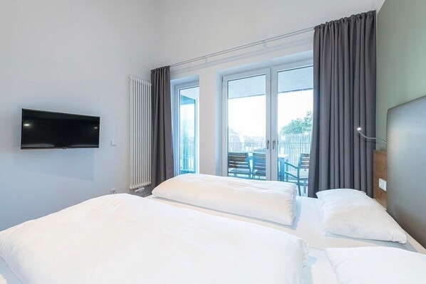 Une chambre d’hôtel avec deux lits, un téléviseur fixé au mur et une vue sur le balcon extérieur.