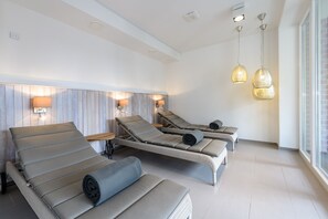 A spa room with three reclining chairs, a wooden headboard, wall-mounted lamps, and pendant lights.
