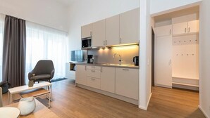 A modern kitchen with a microwave, coffee maker, and cabinets. There is a seating area with a chair and a small table.