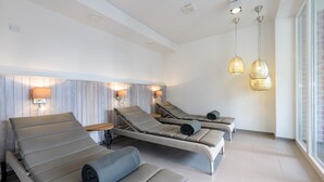 A spa room with three reclining chairs, a wooden headboard, wall-mounted lamps, and pendant lights.