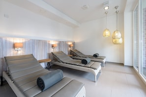 Un cuarto de spa con tres sillas reclinables, un cabecero de madera, lámparas de pared e iluminación colgante.