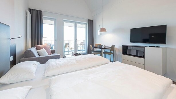A hotel room with a bed, a desk, a television, and a balcony with a view.