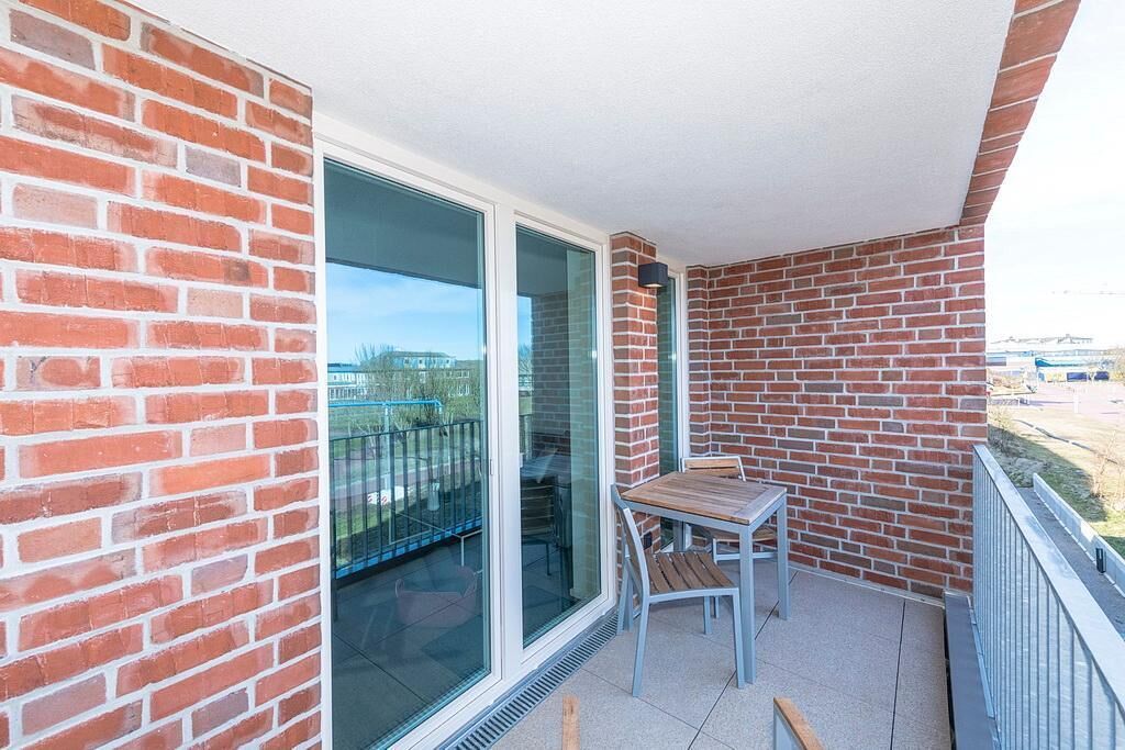 Un balcon avec un mur en briques, une porte vitrée et une petite table avec des chaises.