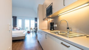 A modern kitchen with a built-in microwave, a sink, and a coffee maker. There is a dining area with a table and chairs visible in the background.