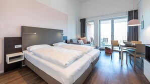 A hotel room with two beds, a desk, a chair, and a dining table.