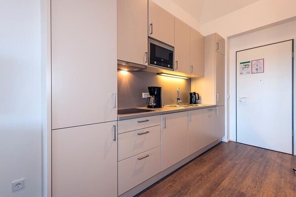 A modern kitchen with white cabinets, a microwave, a coffee maker, and a sink.