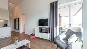 A modern living room with a flat-screen TV, a grey armchair, a white bench, and a small potted plant.