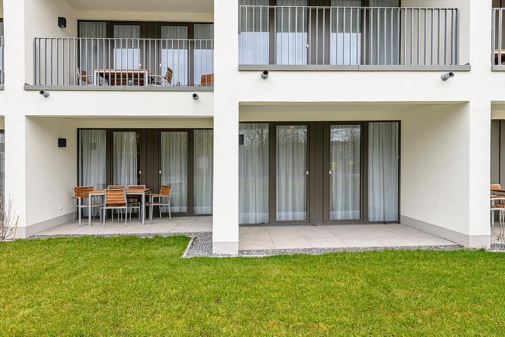 A modern apartment building with balconies, a patio area with a table and chairs, and large sliding glass doors.
