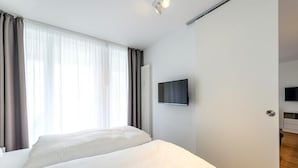 Une chambre d’hôtel avec deux lits, un téléviseur à écran plat fixé au mur et une fenêtre avec des rideaux.