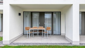 Une terrasse extérieure moderne avec une table et des chaises, un espace couvert doté de portes-fenêtres coulissantes et un mur extérieur blanc.