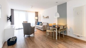 Un salon moderne avec un canapé, une table à manger et des chaises. Un téléviseur est fixé au mur et un radiateur se trouve à droite.