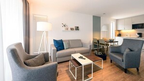 Un salon moderne comprenant un canapé, deux fauteuils, une table basse et un coin repas avec une table et des chaises.