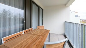 Un balcon avec une table et des chaises en bois, de grandes fenêtres et une vue sur l’extérieur.