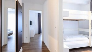 Une chambre d’hôtel avec un lit superposé, une armoire et une salle de bain visible à travers une porte ouverte.