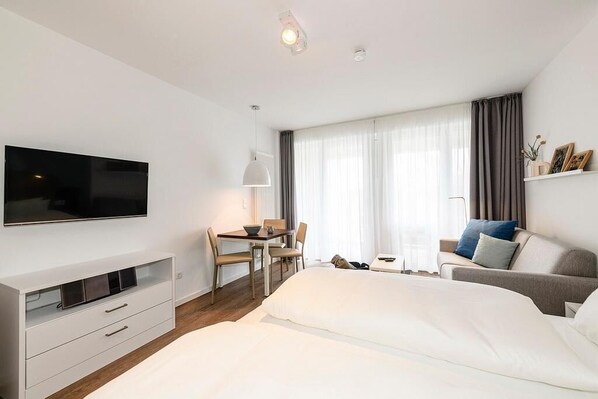 A modern hotel room with a bed, a desk, a chair, a television, and a window with curtains.