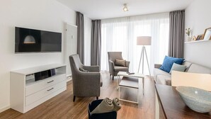 A modern living room with a flat-screen TV, two armchairs, a sofa, a coffee table, and a floor lamp.