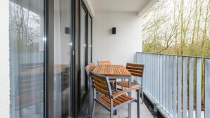 A balcony with a table and chairs, a glass door, and a view of trees.