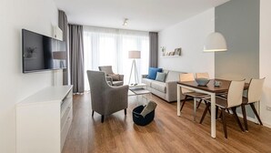 A modern living room with a flat-screen TV, a sofa, a dining table with chairs, and a floor lamp.