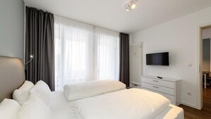 A hotel room with a large bed, a TV on the wall, and a window with curtains.