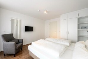 Una camera da letto moderna con un letto, una poltrona grigia, una televisione e un armadio bianco.