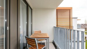 Un balcón con una mesa y sillas de madera, barandilla metálica y vistas de la ciudad.