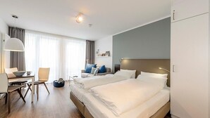 Habitación de hotel con dos camas, un escritorio con silla, una mesa de comedor y un ventanal con cortinas.