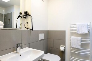 Ein modernes Badezimmer mit einem weißen Waschbecken, einer Toilette, einem Handtuchhalter mit weißen Handtüchern und einem an der Wand befestigten Föhn.
