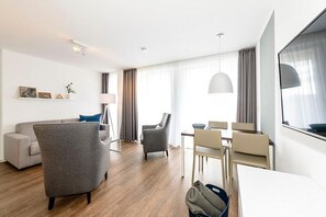 A modern hotel room with a sofa, armchair, dining table, and chairs.