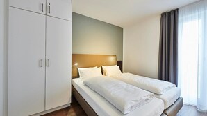 Una habitación de hotel con cama doble, un armario y un gran ventanal con cortinas.