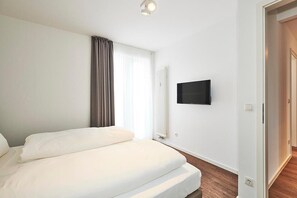 Ein Hotelzimmer mit einem großen Bett, einem flachbildfernseher an der Wand und einem Fenster mit Vorhängen.