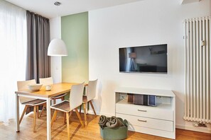 Una habitación moderna con una mesa de comedor de madera, sillas blancas, un televisor en la pared y un radiador.