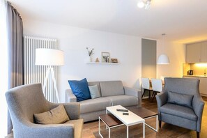 Una sala de estar moderna con un sofá gris, dos sillones, una mesa de centro y una zona de comedor con sillas.