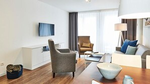Ein modernes Wohnzimmer mit einer Couch, Sesseln, einem Couchtisch und einem an der Wand befestigten Fernseher.