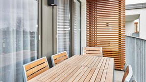 Ein moderner Essbereich im Freien mit Holztisch und -stühlen, einer Glastrennwand und einer Wand aus Holzlamellen.