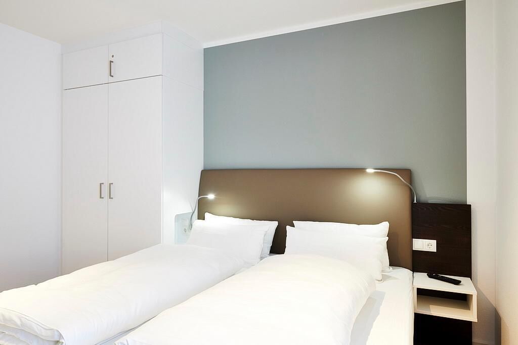Une chambre d’hôtel comprenant un lit, une table de chevet, une armoire et une lampe fixée au mur.