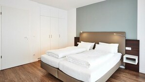 A modern bedroom with a large bed, white wardrobe, and a bedside table. - Apartment mit Zwei Balkonen Inkl. Schwimmbad- & Saunanutzung in Strandnähe (Nordseeheilbad Bensersiel)
